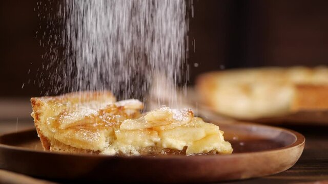 Powdered sugar spilling on plate with piece of yummy apple pie in kitchen at home