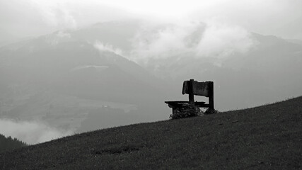 Fototapeta premium old wood bench on a field with view to the alps on a rainy day 