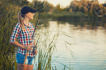 Cute caucasian woman is fishing with rod on the summer lake on the sunset