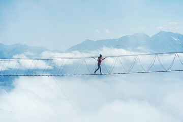 A person walks on a suspended rope bridge in the clouds. Extreme attraction. - Powered by Adobe
