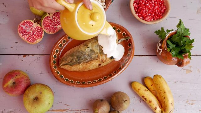 Preparation of the Chile en Nogada a typical mexican dish with the addition of nogada sauce made with nuts, pomegranate seeds and parsley in traditional clay plate