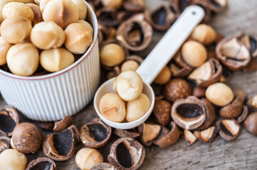 Organic Macadamia nuts with shell on spoon and cup on wood table