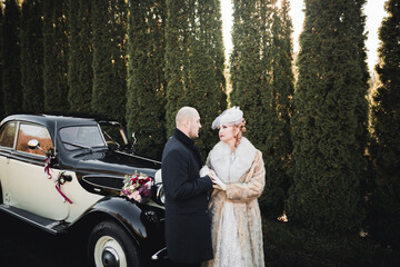 Happy newlywed couple, man and wife kissing near stylish retro car