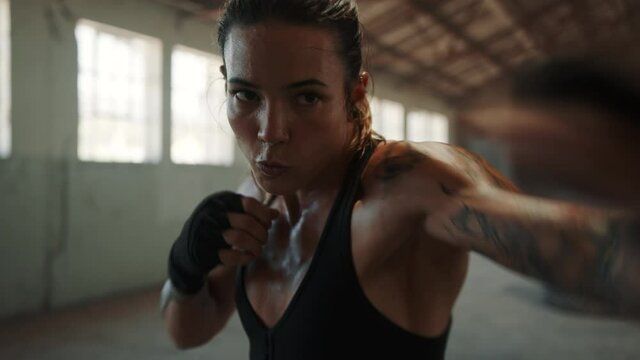 Female doing shadow boxing workout inside old warehosue. Woman in sportswear practicing her punches at a fitness space inside abandoned warehouse.

