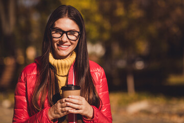 Photo of positive cheerful girl stand copyspace hold takeaway latte cup enjoy fall park promenade...