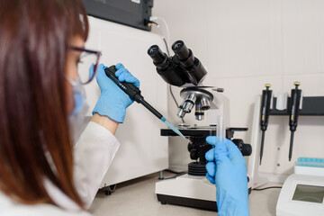 Young woman doctor laboratory assistant is using micropipette test tubes near a medical microscope.