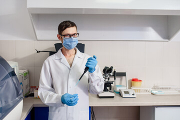 In the hospital laboratories working process, a young man doctor scientists is using micropipette...