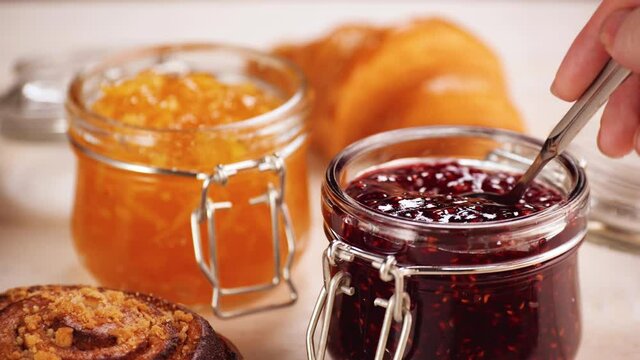 High angle of crop person taking delicious raspberry jam from glass jar during breakfast