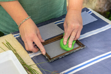 Woman holding frame for making paper sheets from waste paper pulp. Selective focus. Decorative and applied art. Recycling concept, ecology.