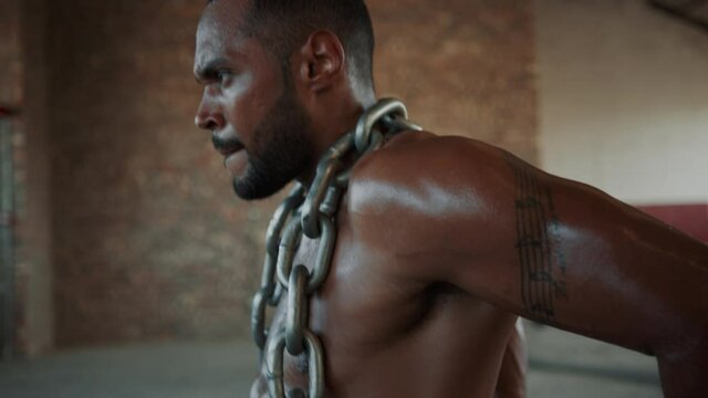 Fitness man doing triceps dip exercises with a chain around his neck.  Strong man doing intense workout at cross training space in old warehouse.
