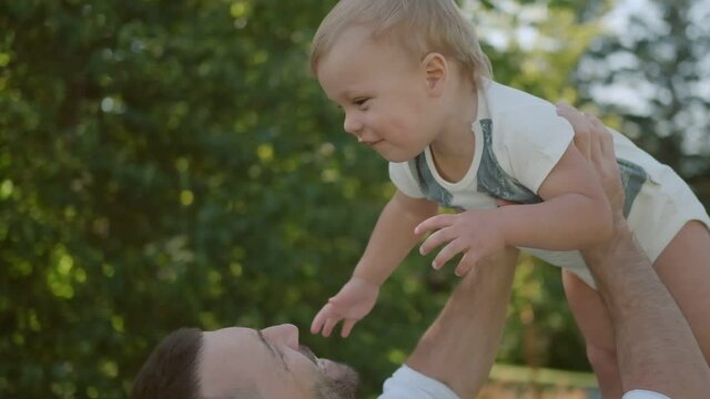 young father holds his little son in his arms and smiles. father with child outdoors in the park. relationship and love of parents and children