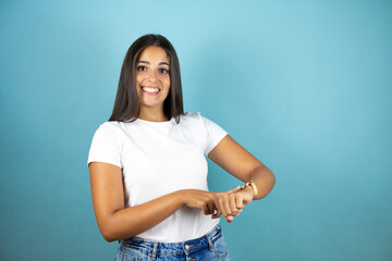 Fototapeta na wymiar Young beautiful woman standing over isolated blue background smiling and pointing her watch 