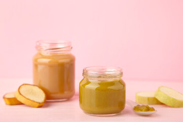 Glass jars with nutrient baby food on pink background