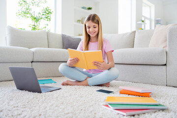 Full size photo of positive girl kid study remote read book online lesson school task prepare home task sit carpet floor legs cross ed in house weekend indoors