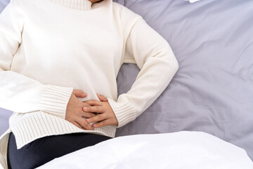 Young woman suffering stomach aches lying on the bed. Healthcare medical or daily life concept.