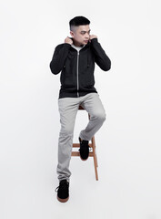 Young handsome man wearing black zip hoodie was sitting in a chair while posing isolated on background suitable for mockup