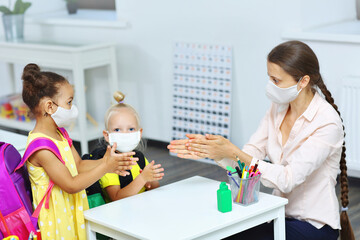 a teacher and students in medical masks learn hand disinfection in the classroom
