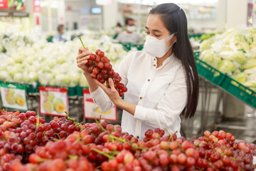 Asian woman long hair wearing protective face mask  in supermarket department store. Female, looking grocery to buy  some fruit. New normal after covid-19. Family concept. Soft focus photo.