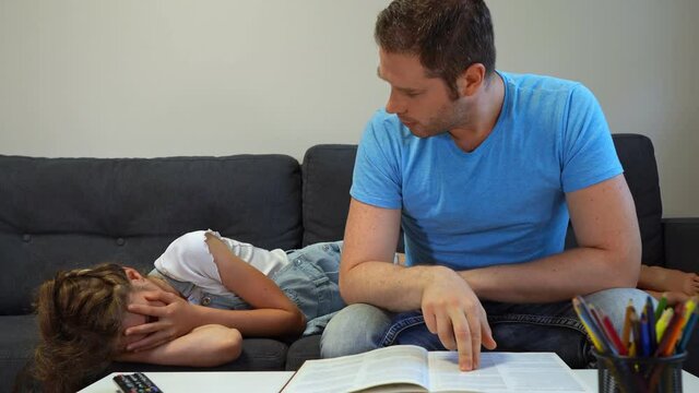 Dad reads a book, but his daughter is not interested and crying.
