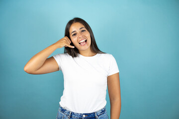 Young beautiful woman over isolated blue background smiling doing phone gesture with hand and fingers like talking on the telephone