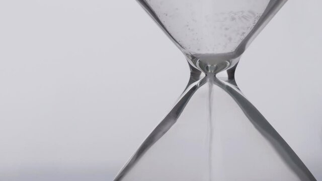 Close-up detail of sand pouring in hourglass, time pass concept, deadline end