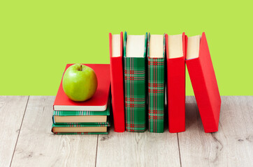 Back to school, pile of books in colorful covers and green apple on wooden table with lime mint green background. Distance home education. Quarantine concept of stay home.