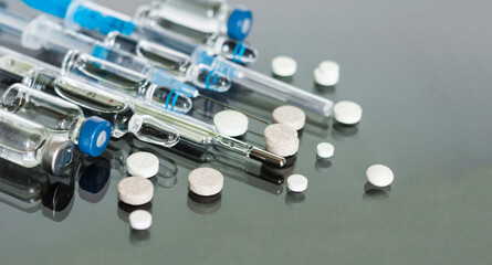 Thermometer, pills, injection vaccineampoules, syringe for vaccination on glass background,...