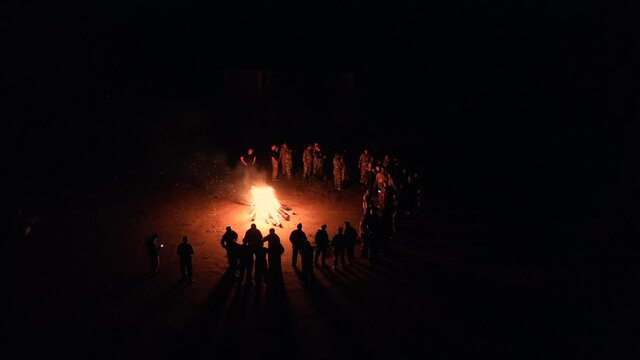 Group of friends stands in a semicircle around the fire and sings songs