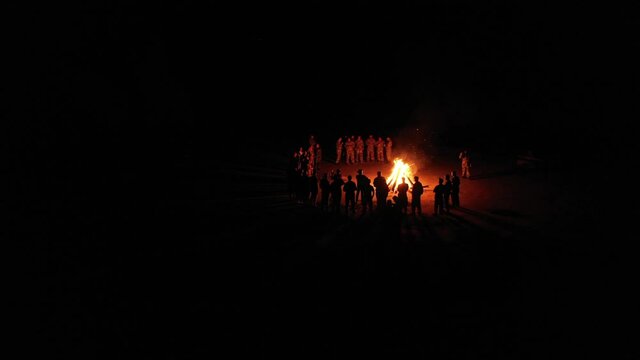 Group of friends stands in a semicircle around the fire and sings songs