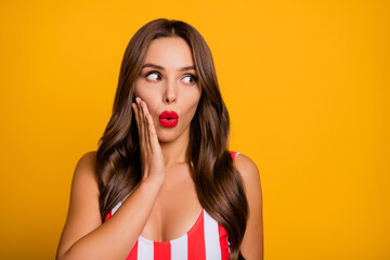Photo of attractive lady perfect bronze tanned body skin open mouth red lips look interested side empty space arm on cheek wear striped bodysuit isolated bright yellow color background