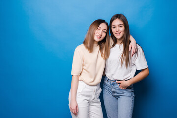 Friends forever. Two cute lovely girl friends posing with smile on blue background