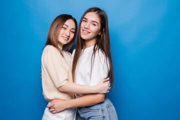Two woman friends hug each other isolated blue color background
