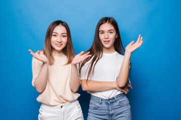 Two beautiful surprised with their hands up, dressed in casual clothes on a blue background. People emotions concept.