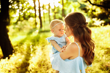 Lovely mother gently holds little baby girl in arms, walking at the park, caring parent try to kiss...