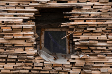 A tall woodpile consisting of a lot of wood stacked around the window