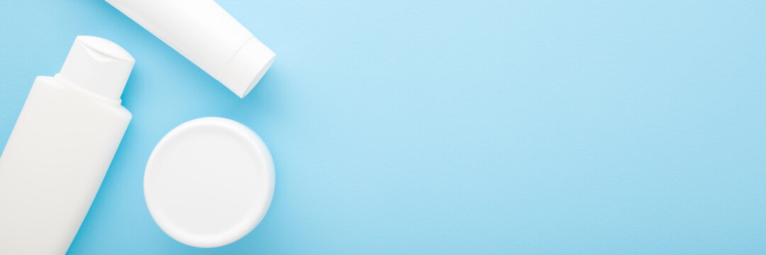 White plastic bottle, tube and jar on light blue table background. Pastel color. Care about face, hands, legs and body skin. Women and men beauty products. Empty place for text or logo. Top down view.