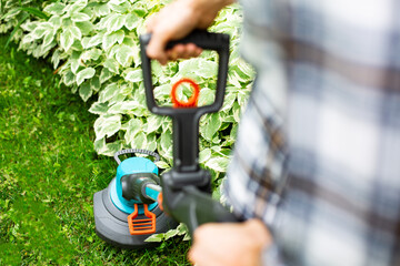 Cutting the lawn with cordless grass trimmer, edger, focus on trimmer. Gardening.