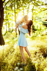 Beautiful woman with baby girl walking at the park, lovely mother kissing adorable daughter, caring parent lifts in air cute toddler, enjoy happy family moments, weekend outdoors, parenthood concept