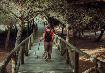 Blond woman walking with her dogs on a wooden pathway in a pinewood in Rota, Cadiz, Spain. © Mlle Sonyah