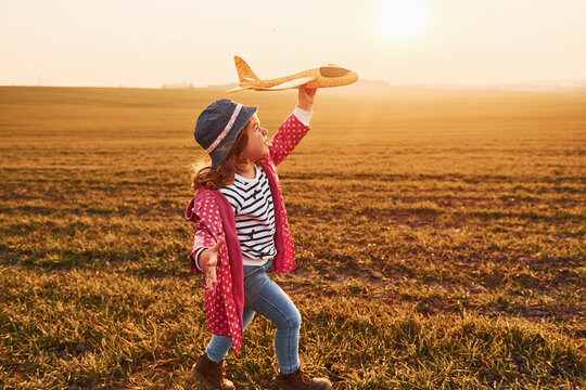 Cute little girl runs with toy plane on the beautiful field at sunny daytime