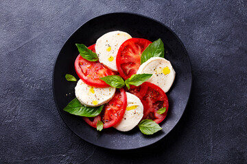 Caprese salad with tomatoes, mozzarella cheese, basil. Dark background. Close up. Top view.