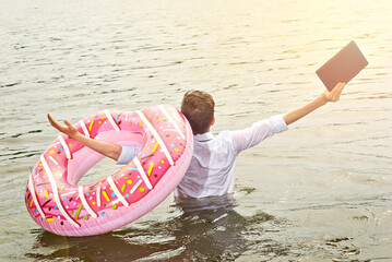 A man in a shirt on a pink inflatable circle. Guy with a laptop swims in the river. The concept of...