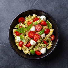 Pasta fusilli with mozzarella cheese, tomatoes and basil. Dark background. Close up. Top view.