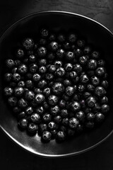 Bilberry in a black plate on black background, top view