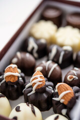 Primer plano de bombones de chocolate con leche, chocolate blanco y chocolate amargo, acomodados en una caja con decoración por encima 
