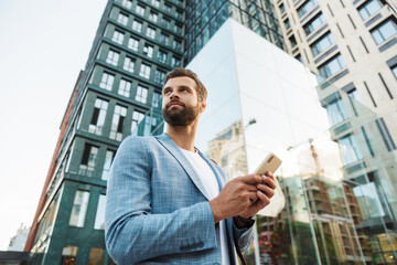 Image of young handsome businessman holding cellphone outdoors