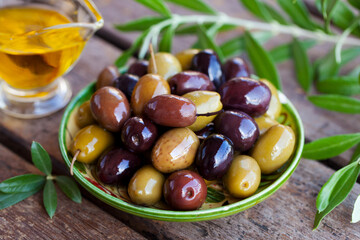 Assortment of fresh olives on a plate with olive tree brunches. Wooden background. Close up.