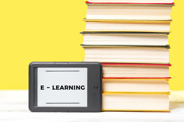 E-learning. E-book reader and a stack of books on a yellow background. Copy space. Concept of education and electronic gadgets
