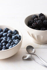 Blueberries and blackberries close-up in bowls on a white background, ripe juicy berries