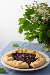 Open pie from shortcrust pastry with black currant, delicious jostaberry galette on the table, wildflowers in a vase